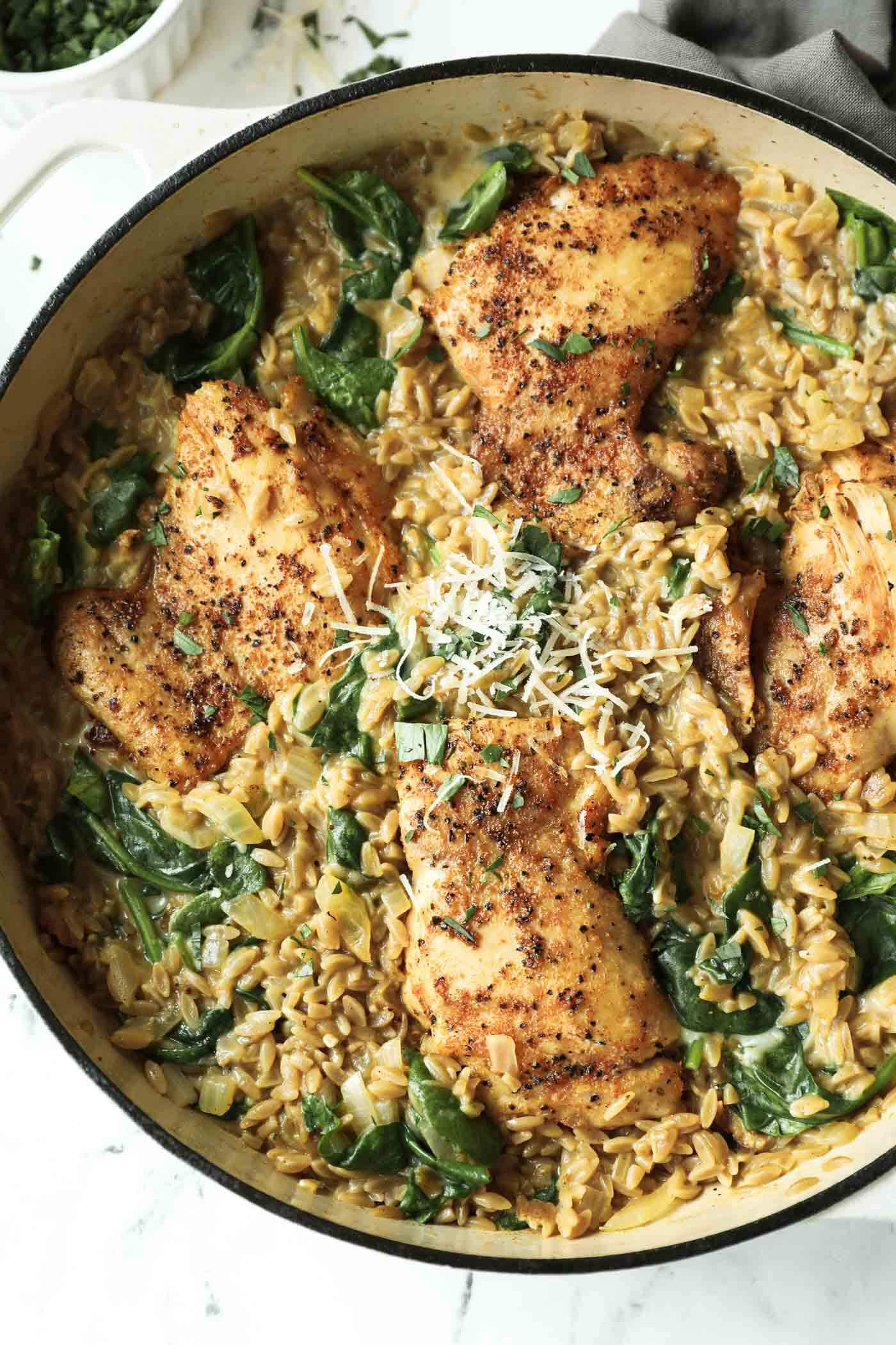 Seasoned chicken thighs served over creamy orzo pasta with spinach, topped with grated cheese, in a large skillet.