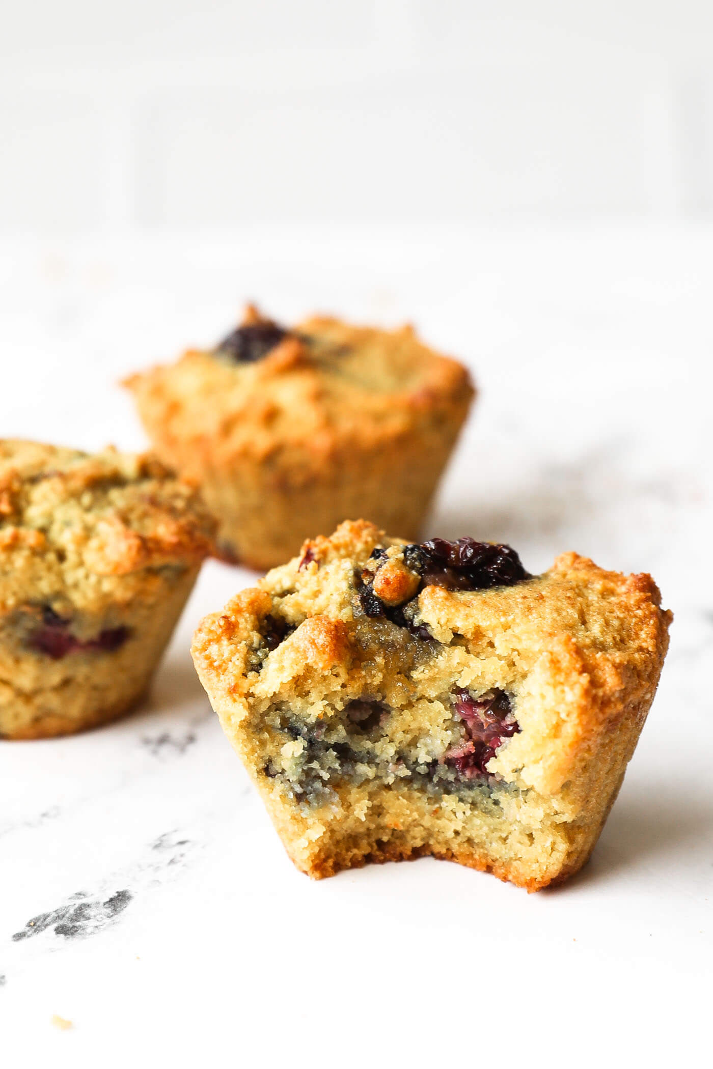 Image of three gluten free blackberry muffins on table. One muffin has a bite taken out of it.