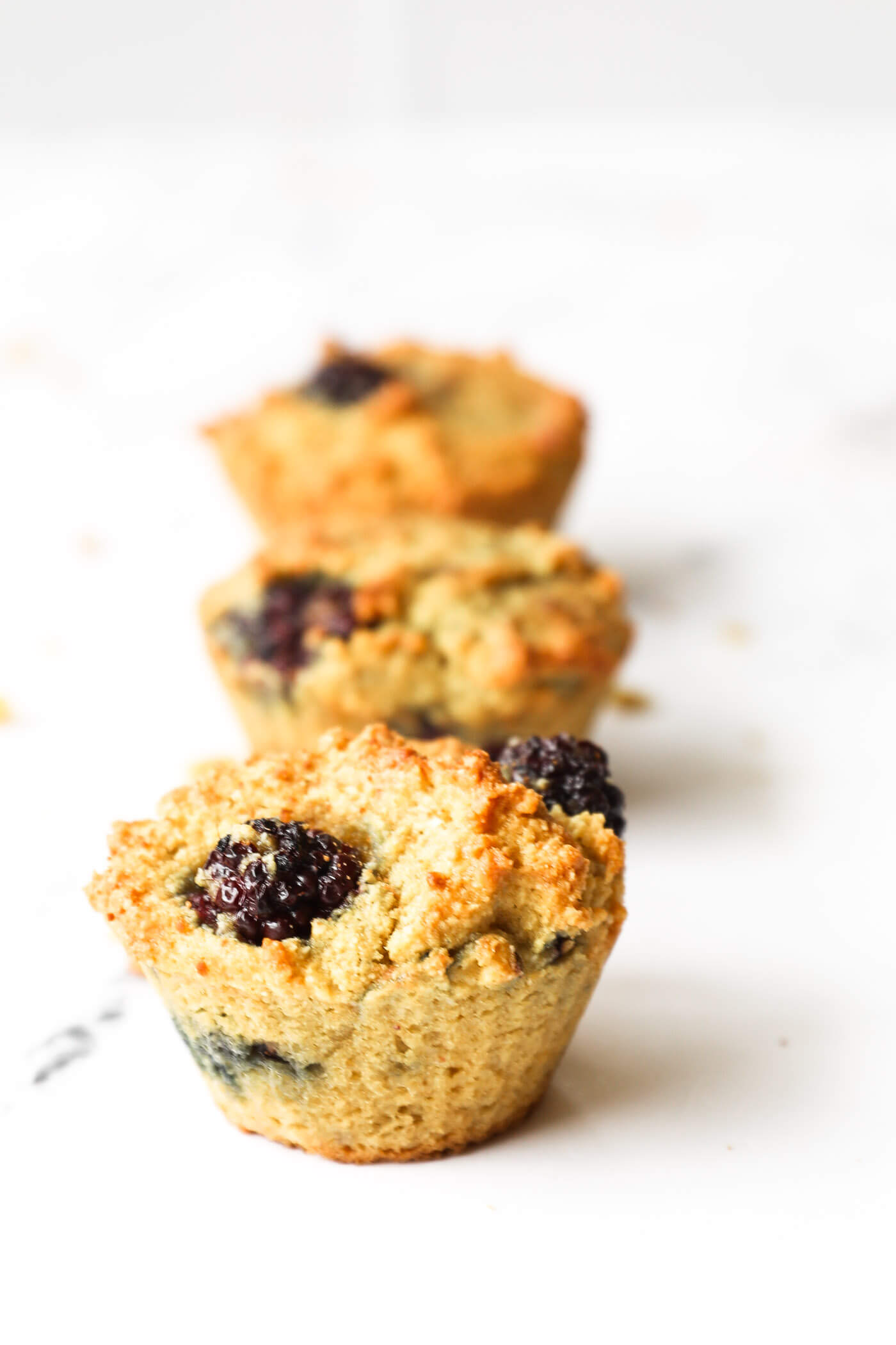 Three blackberry muffins lined up with the front muffin in focus and the other two blurry in the background.