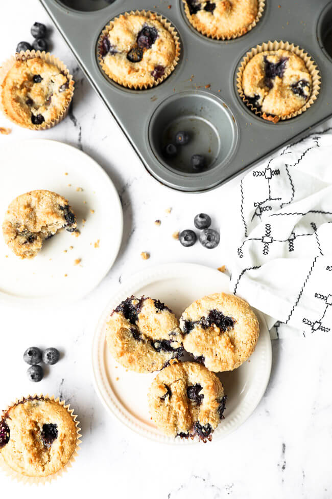 Vertical overhead image of muffins in tin and also on two small plates. One plate has one muffin with a bite taken out of it. The other plate has three muffins. 