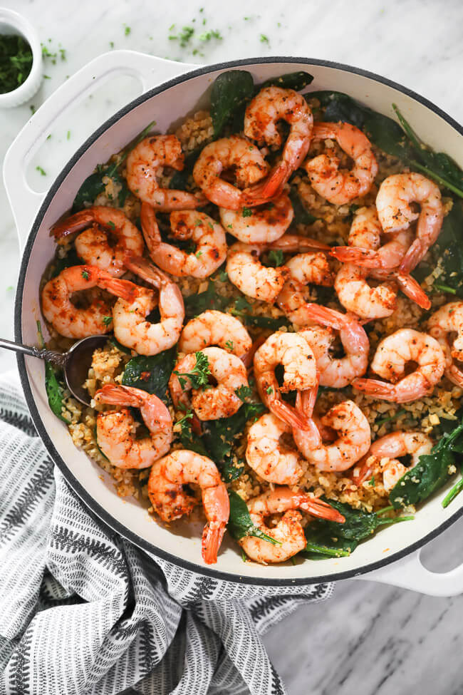 vertical overhead image of cajun shrimp and cauliflower rice in skillet with serving spoon. 