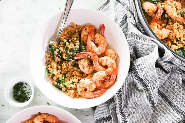 horizontal overhead image of cajun shrimp and cauliflower rice serve up in a bowl with chopped parsley on the side. fork dug into bowl. 