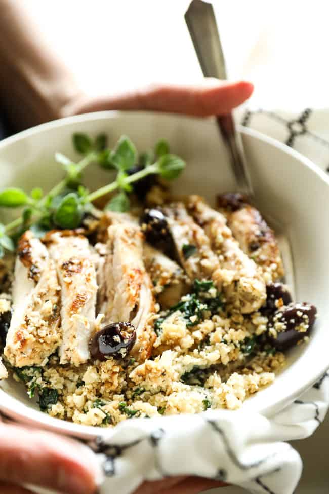 Close up vertical angled shot of holding bowl with greek chicken and fork in the bowl. 