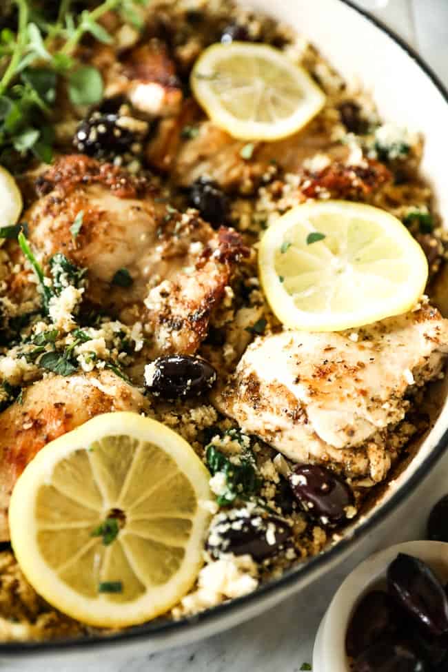 Close up vertical angled shot of greek chicken in a skillet with lemon slices on top. 