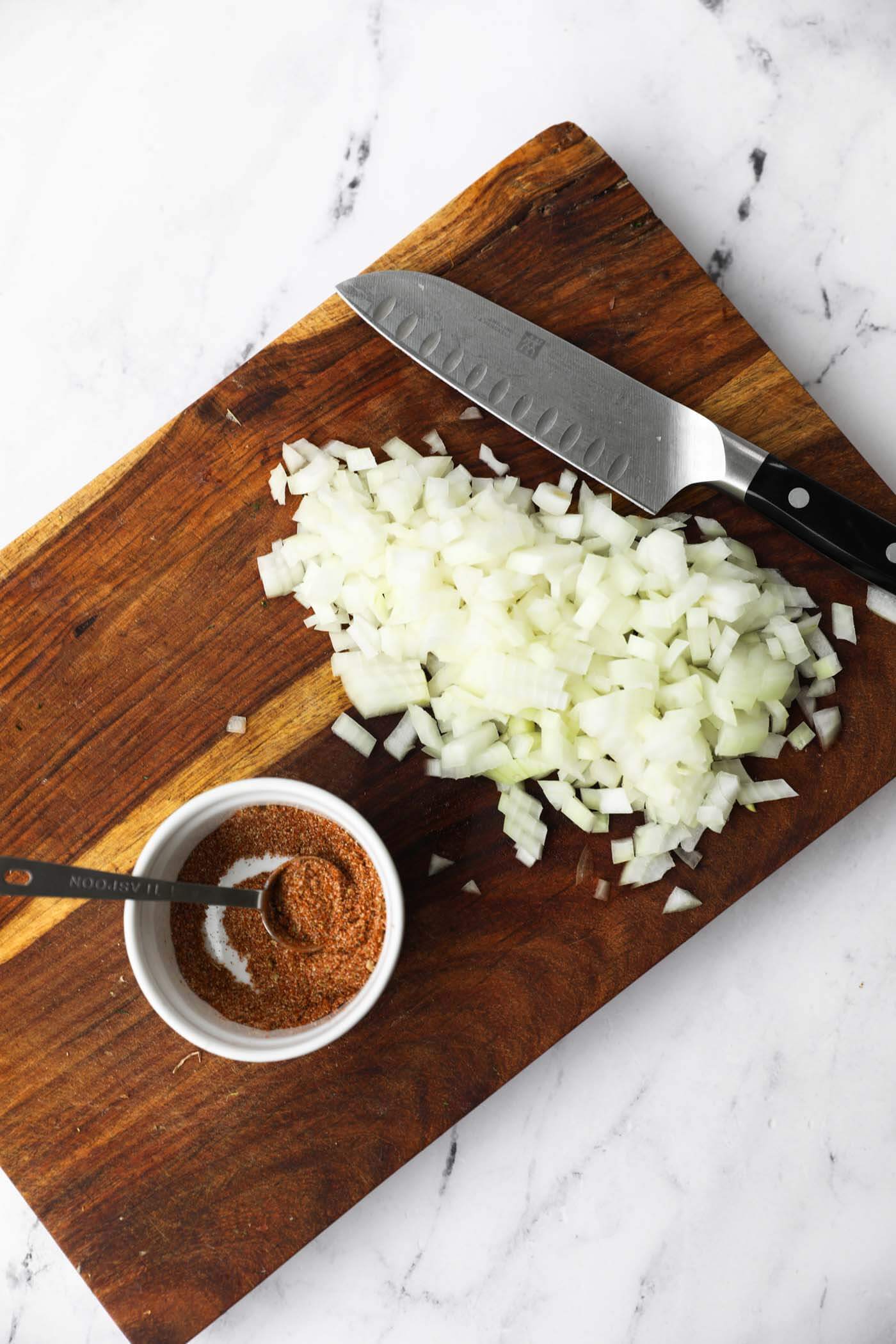 Overhead image of chopped onion and a ramekin of seasonings on a cutting board. 