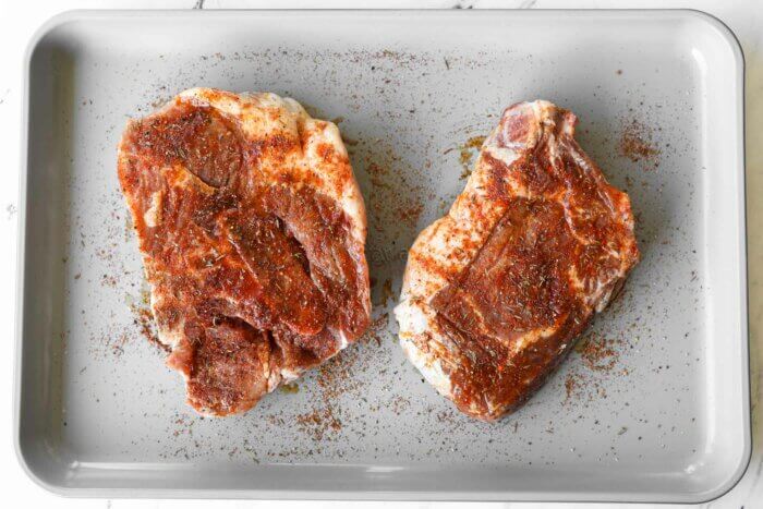Bone in pork chops on a baking sheet with seasoning all over