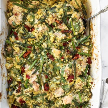 Creamy spinach artichoke chicken casserole in a casserole dish with a serving spoon dug in.