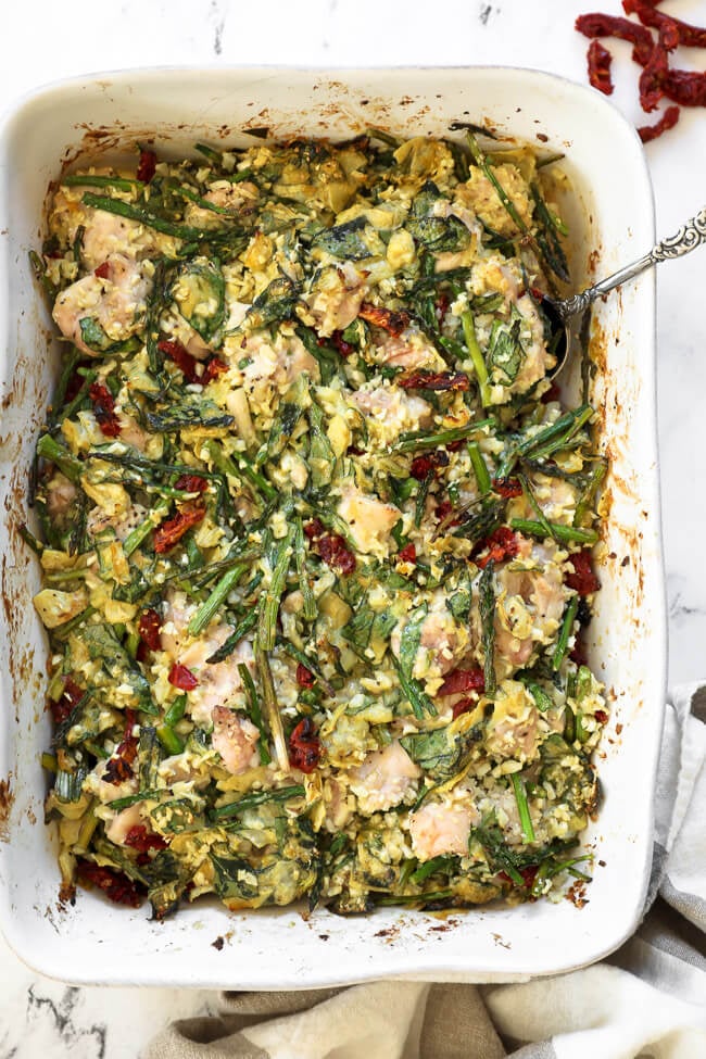 Overhead image of spinach artichoke chicken casserole in casserole dish with a serving spoon. 