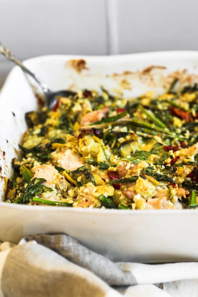 Angled image of spinach artichoke chicken casserole in dish with a serving spoon dug in. 