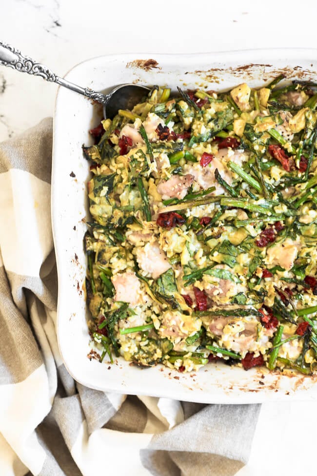 Overhead image of spinach artichoke chicken casserole in casserole dish with a serving spoon. 