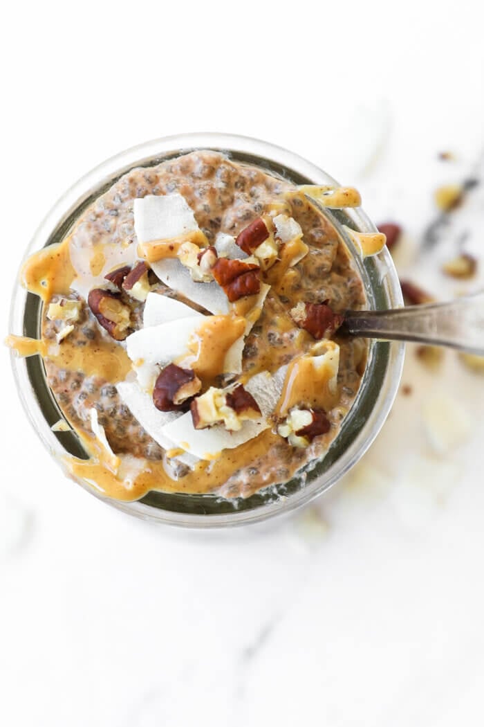 Overhead image of chia pudding in a jar, loaded with toppings like peanut butter, chopped pecans and coconut flakes.