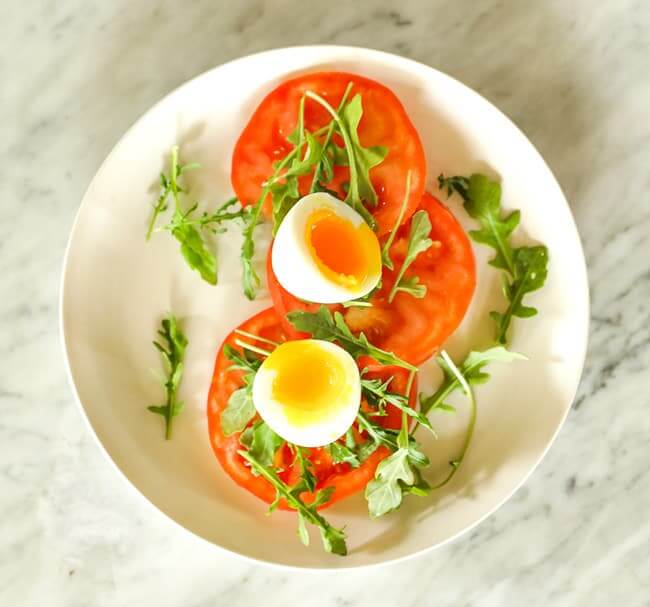 Sliced tomato topped with arugula and soft boiled egg on a plate