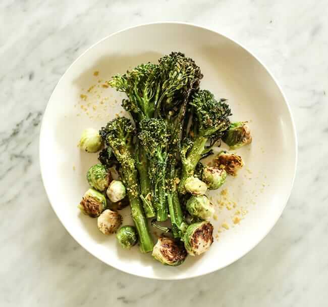 Roasted broccolini and brussels sprouts with nutritional yeast topping on a plate