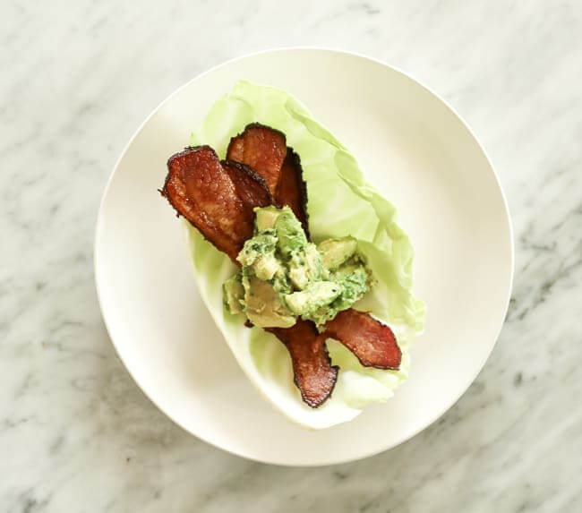 Cabbage leaf topped with bacon and guacamole on a plate