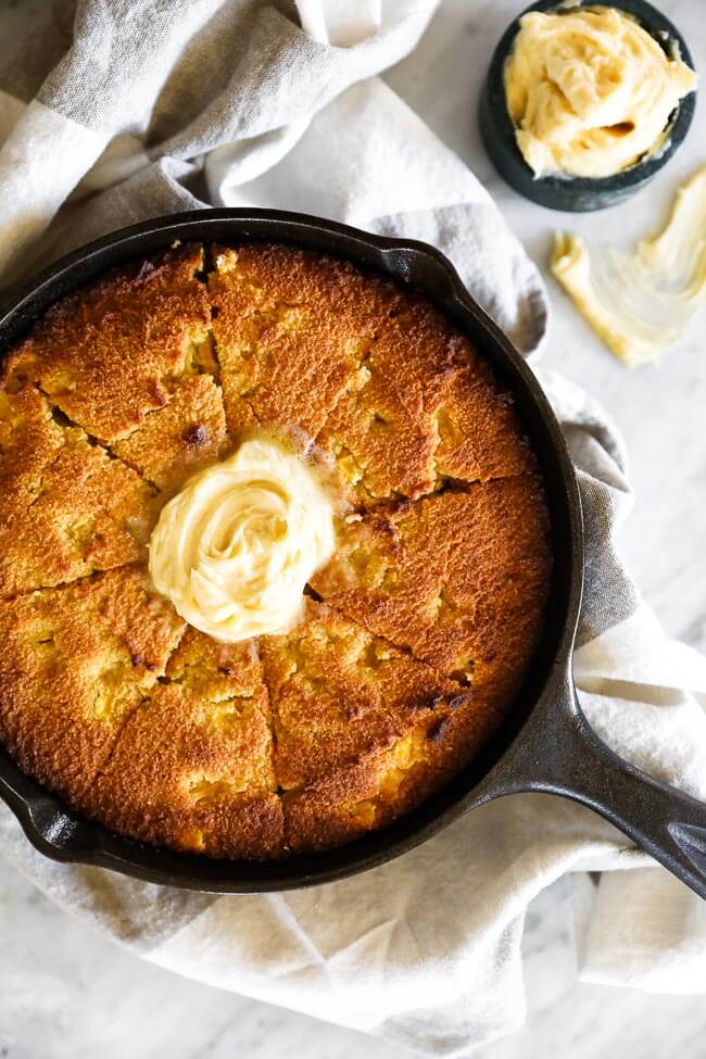 Paleo cornbread in a skillet. Cut into pieces with a big dollop of whipped honey butter on top. 