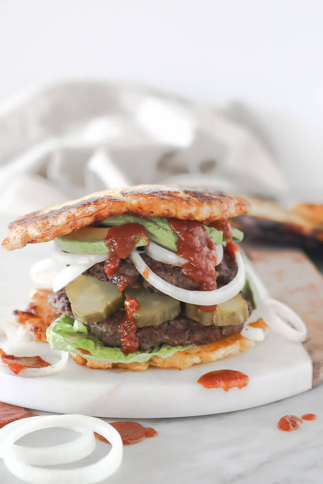 Paleo burger with plantain bun on board with avocado, onion pickle and ketchup dripping down. Close up straight on vertical image.
