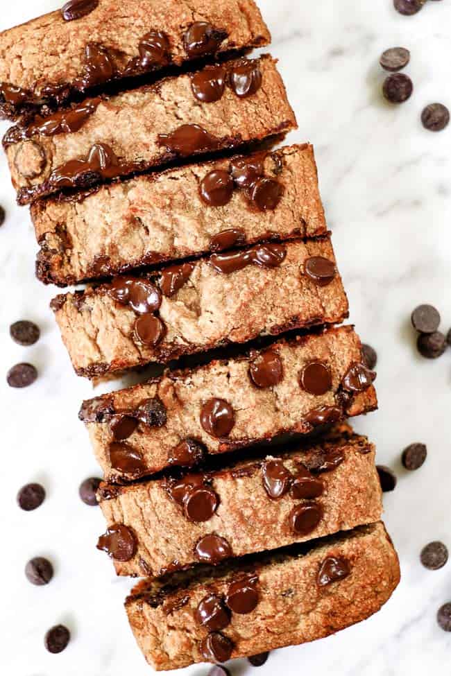 Paleo chocolate chip banana bread sliced loaf on table with extra chocolate chips sprinkled about. 