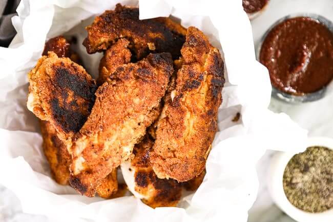 Paleo fried chicken layered in a bowl with parchment paper and BBQ sauce  and pepper on the side. 