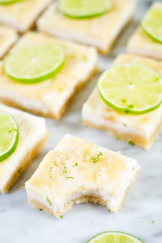 Paleo lime bars topped with lime zest and sliced lime. One bar with a bite taken out of it. 