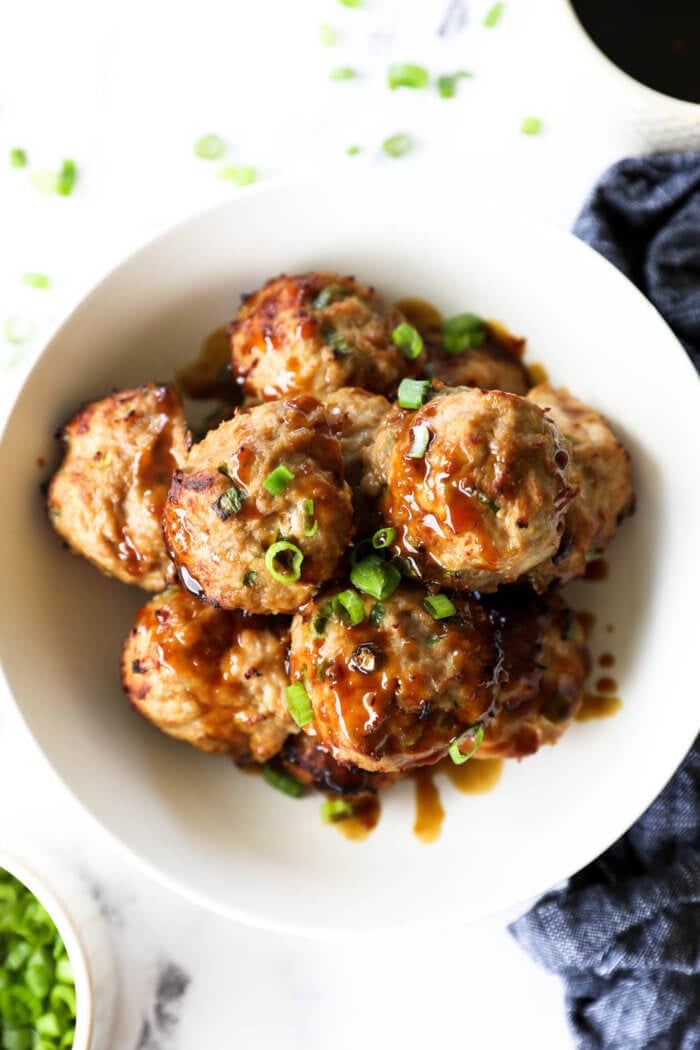 Overhead image of a bowl full of teriyaki turkey meatballs with sticky teriyaki sauce drizzled on top. Garnished with chopped green onion.