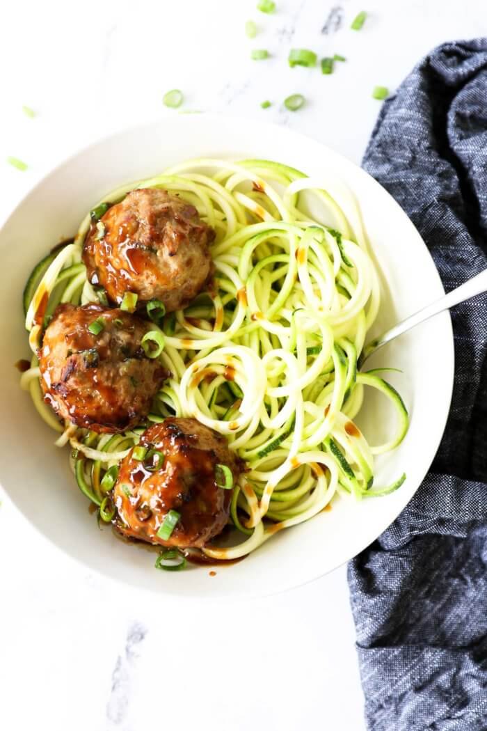 Overhead image of teriyaki meatballs served in a bowl with zoodles and extra teriyaki sauce drizzled on top.
