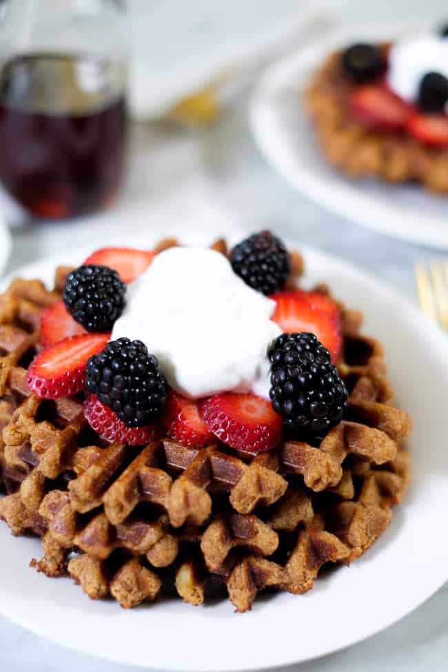 Stack of Paleo waffles topped with berries and coconut whipped cream. 