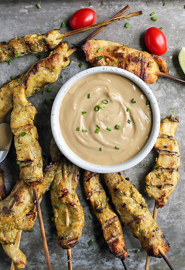 Chicken skewers on a gray background with ramekin of sunbutter sauce in middle