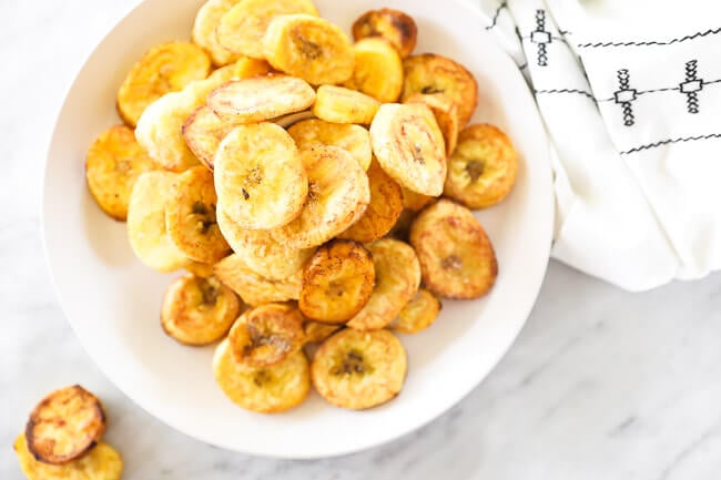 Horizontal overhead image of pan fried green plantains piled up on a plate. 