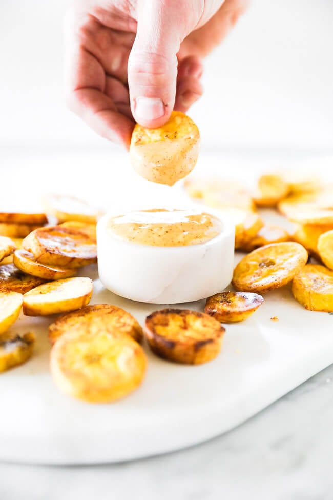 Vertical straight on image of dipping fried plantain into sauce. 