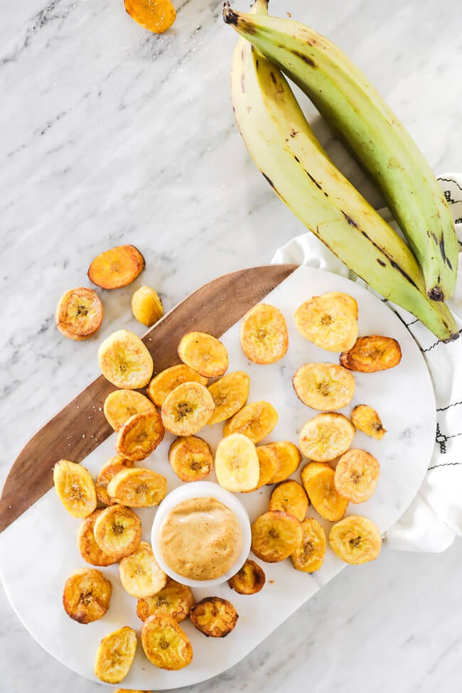Vertical overhead image of pan fried plantains spread out on marble with green plantains on the side. 
