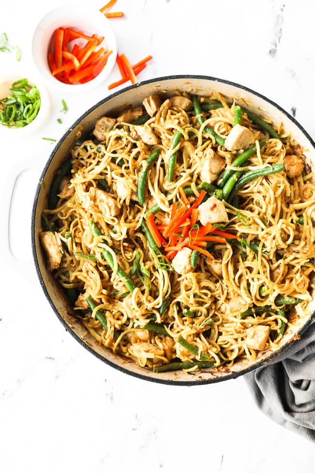 Overhead image of a large skillet with peanut butter chicken and noodles. Topped with chopped red pepper and green onions. 