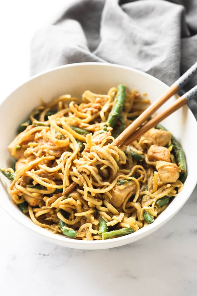 Angled image of peanut butter chicken and noodles in a bowl with some noodles spun around chopsticks. 