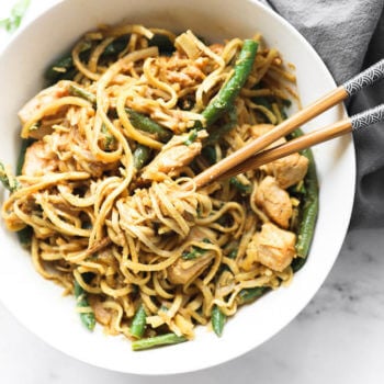 Overhead shot of peanut butter chicken noodles in a white bowl with chopsticks