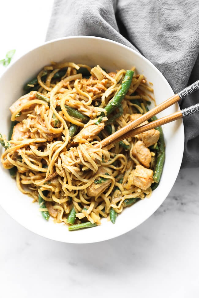 Overhead image of peanut butter chicken and sweet potato noodles in a bowl with some noodles spun around chopsticks. 