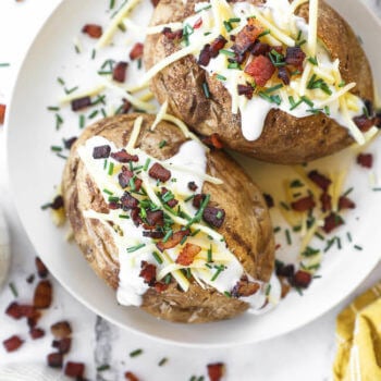 Overhead image of air fryer baked potatoes loaded with sour cream, cheese, bacon and chives