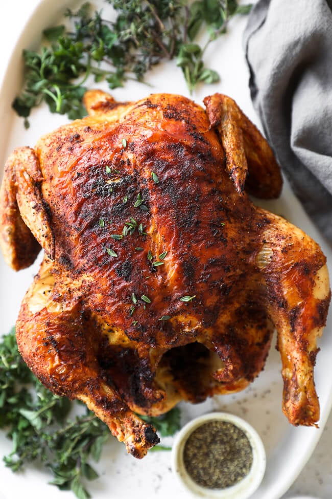 Close up overhead shot of whole air fryer roast chicken on a platter with fresh herbs around it