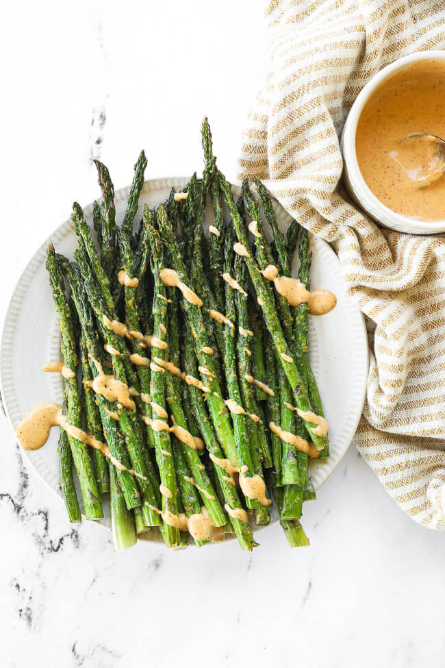 Air fryer asparagus on a plate with chipotle aioli drizzled on top. 