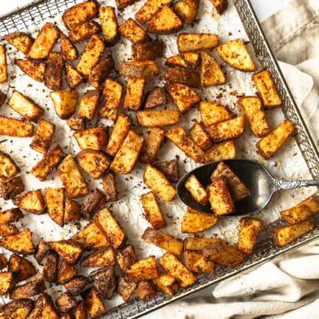 Perfectly seasoned air fryer breakfast potatoes in an air fryer basket with spoonful of potatoes