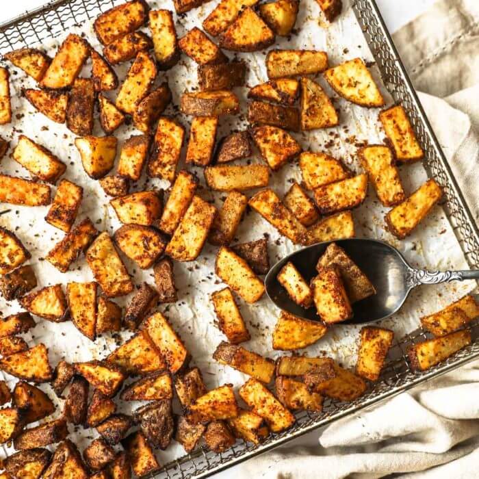 Perfectly seasoned air fryer breakfast potatoes in an air fryer basket with spoonful of potatoes