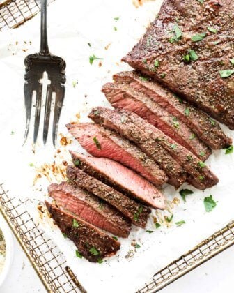 Overhead image of the texture of flank steak sliced into strips with a serving fork on the side. Topped with fresh cilantro on top.