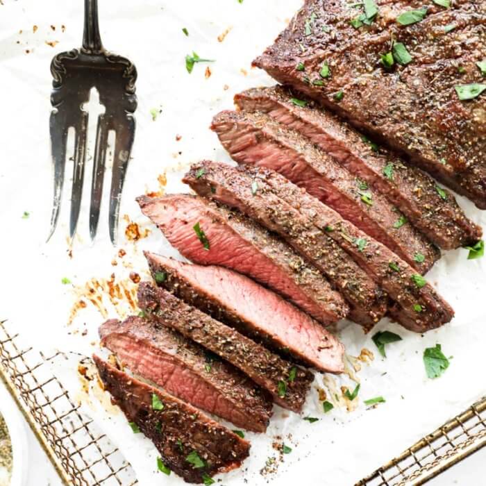 Overhead image of the texture of flank steak sliced into strips with a serving fork on the side. Topped with fresh cilantro on top.