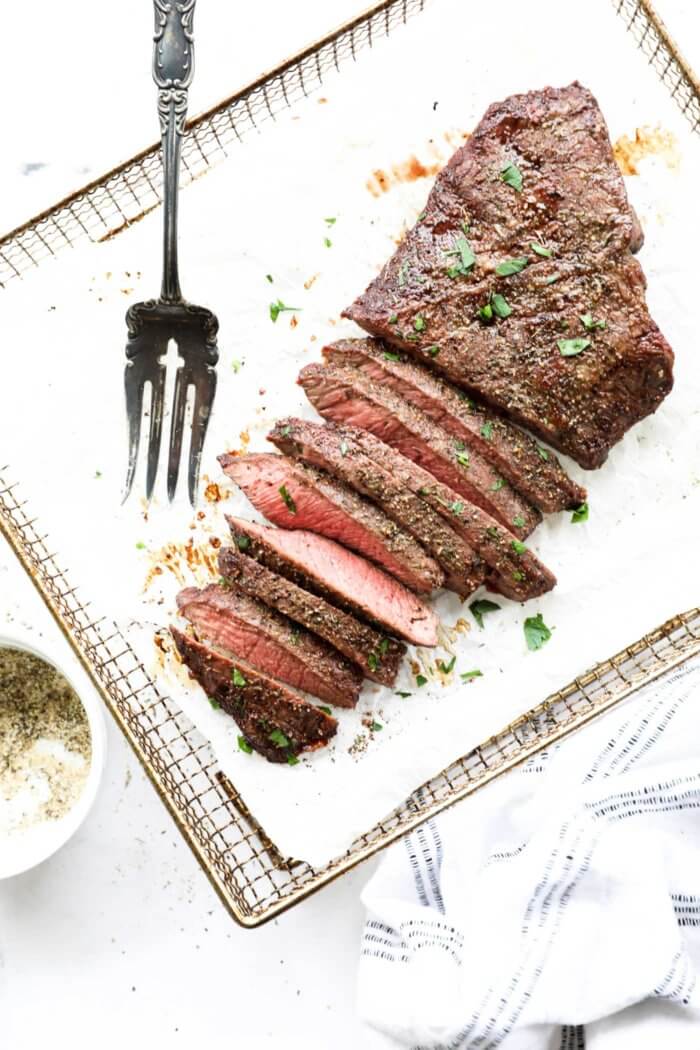 Overhead image of air fryer flank steak sliced into thin strips with a serving fork on the side. Garnished with chopped cilantro on top.