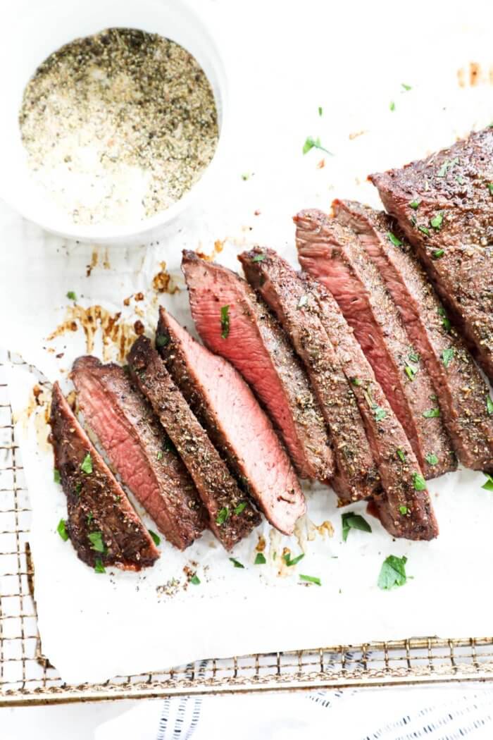 Overhead image of slices of flank steak feathered out with a ramekin of seasoning on the side and fresh cilantro sprinkled on top.