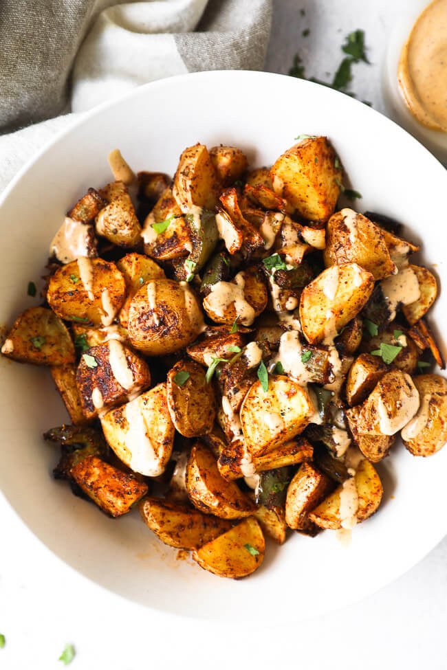 Roasted potatoes in a white bowl with a drizzle of sauce and chopped parsley on top