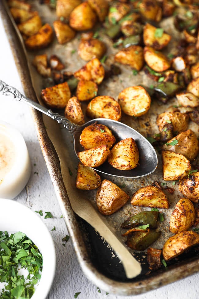 Roasted mexican potatoes on a sheet pan with spoonful of potatoes close up angle image