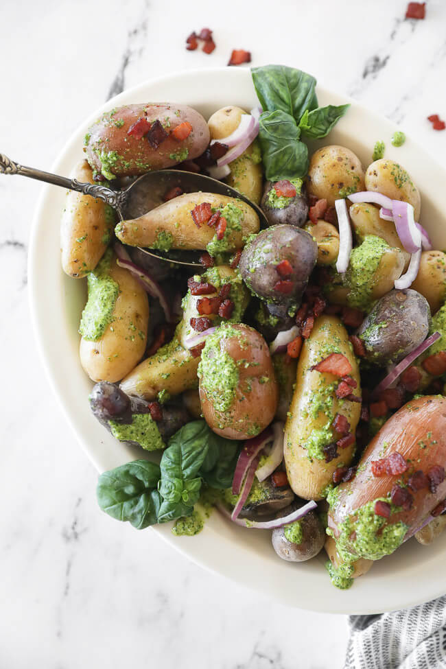 pesto potato salad in bowl with a spoon and bacon sprinkled on top vertical image