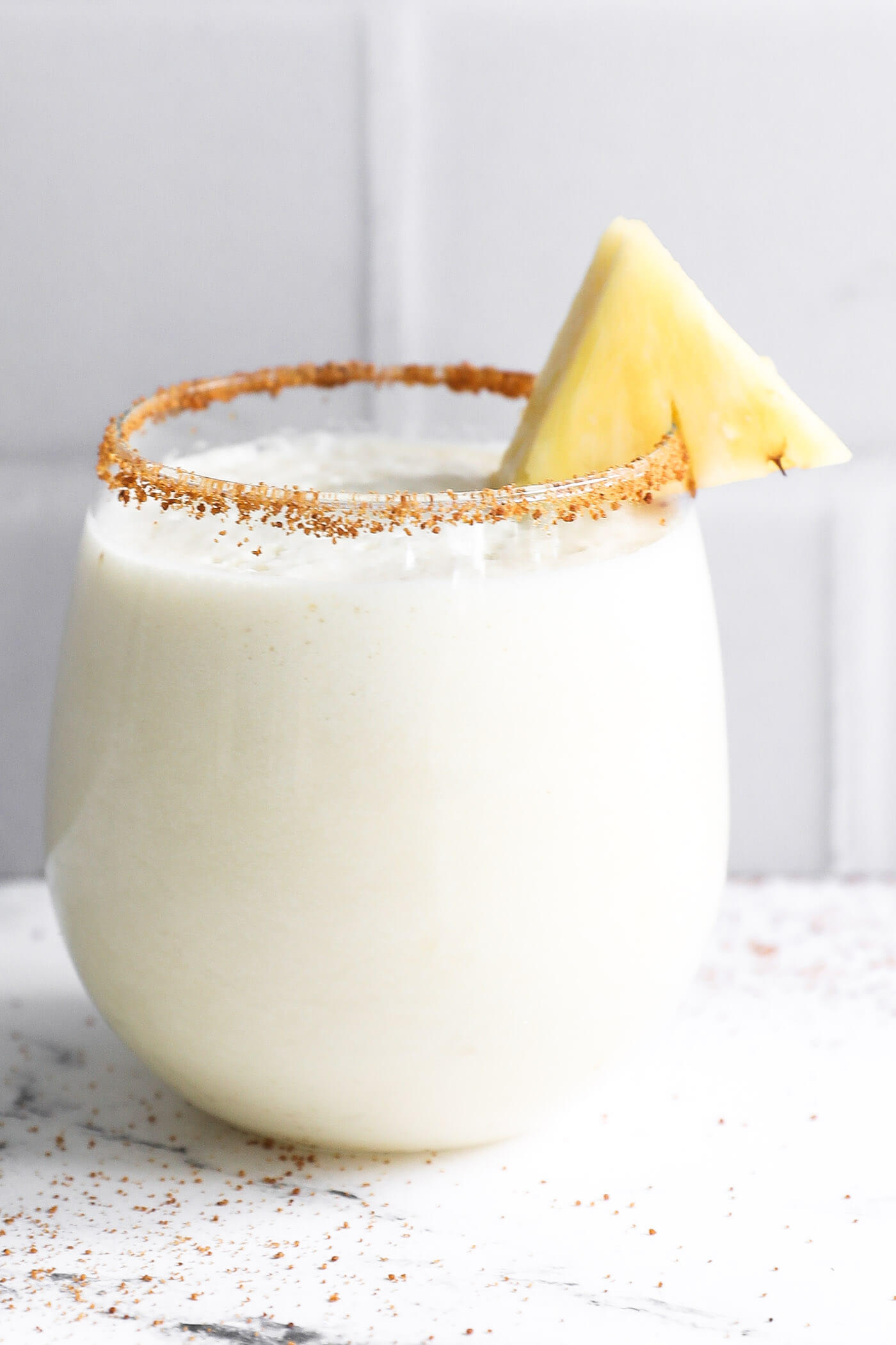 Close up shot of a pina colada mocktail in a glass. The rim is lined with grainy coconut sugar and a slice of pineapple.