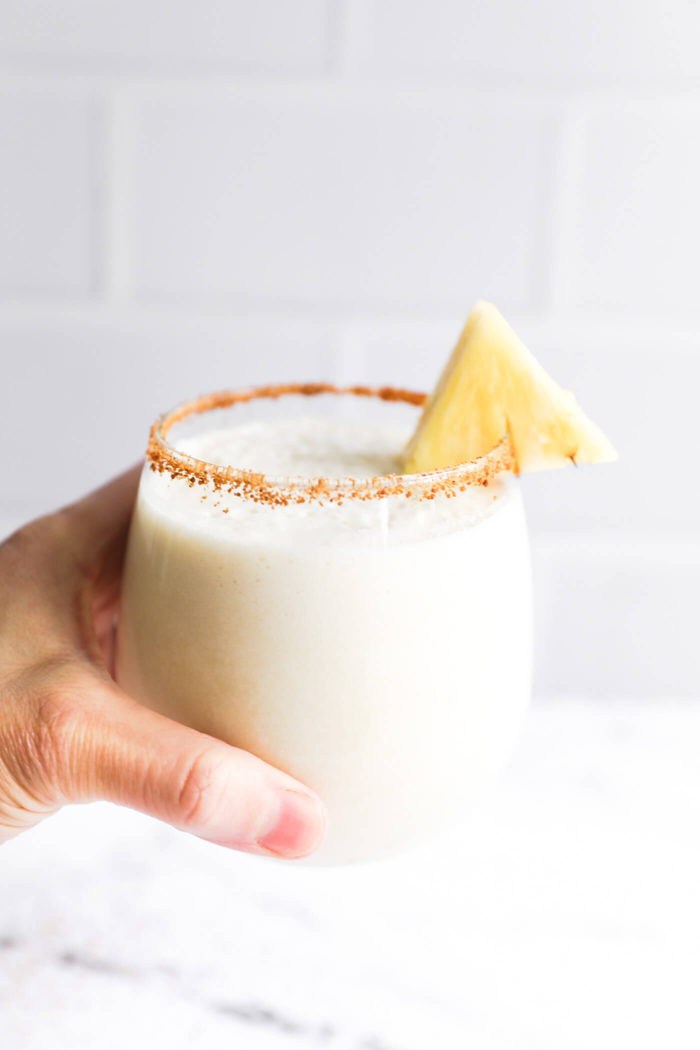 Holding a glass with a pina colada mocktail. Glass is lined with coconut sugar and a slice of pineapple.