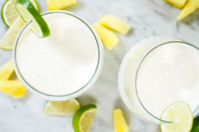 Two glasses of this paleo, dairy-free and refined sugar-free piña colada smoothie garnished with lime slices and pineapple chunks.