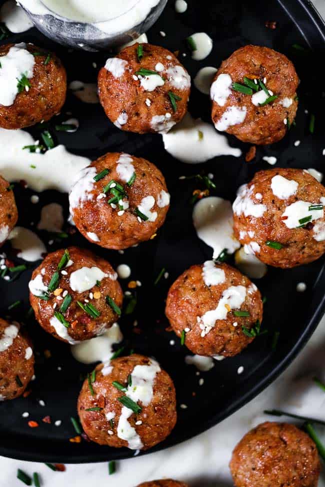 Pork meatballs topped with ranch dressing, chopped chives, red pepper chili flakes and sesame seeds. 